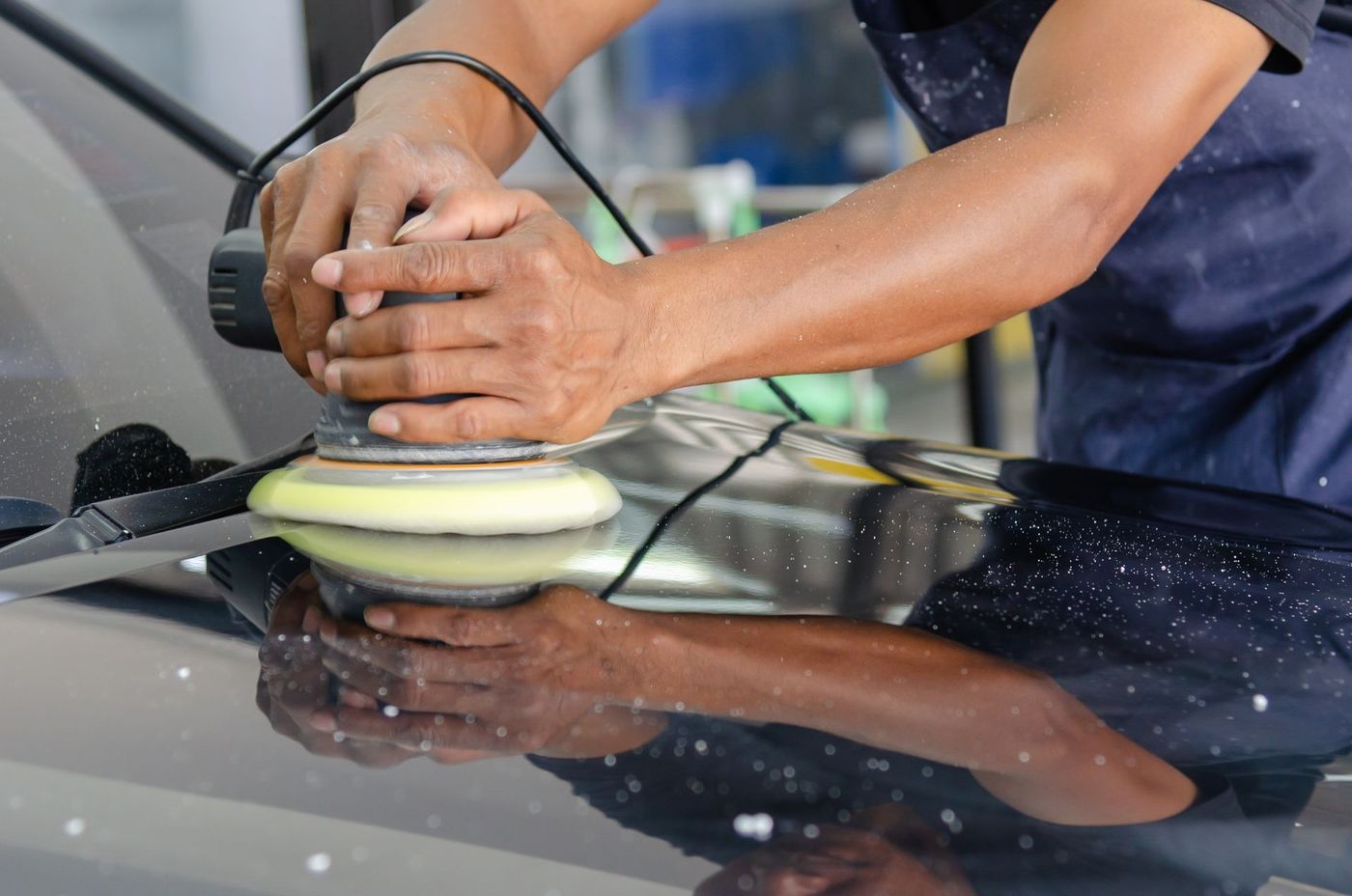 A machine polisher being worked across a car bonnet